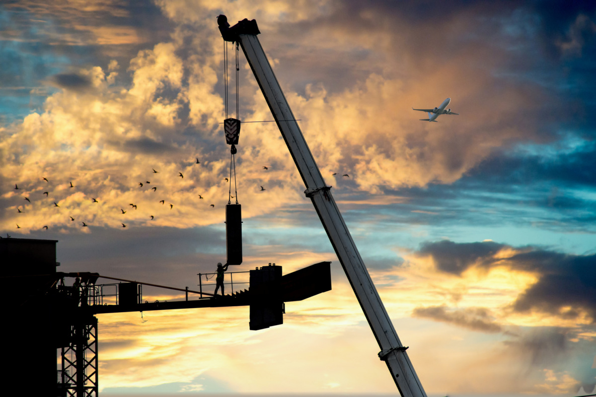 construction crane being built using a secondary crane shot against white sky with the concrete slab counterweight being placed and installed by a man holding it and guiding it in