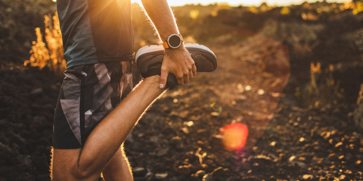 Male runner stretching leg and feet and preparing for running outdoors. Smart watch or fitness tracker on hand. Beautiful sun light on background. Active and healthy lifestyle concept.