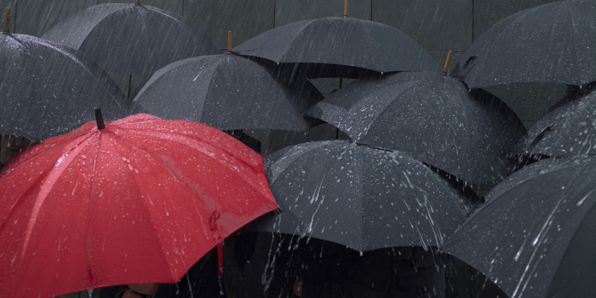 Red umbrella amongst group of open umbrellas in rain